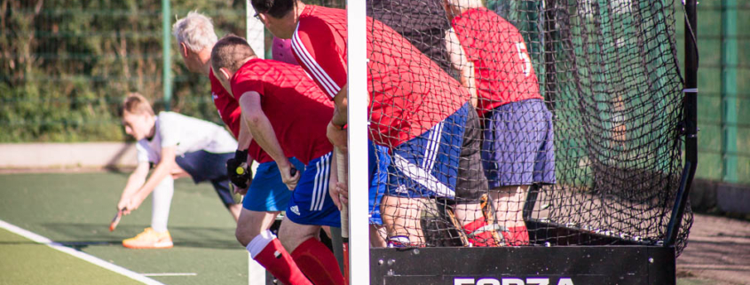 Redditch Hockey Men tucked in the goal to defend a penalty corner in red home kit